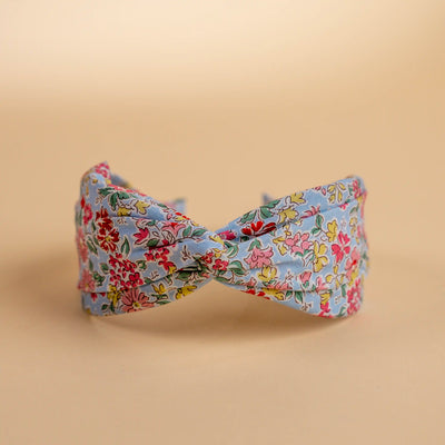 Lucys Light Blue Poppy Floral Headband. Light blue background with pink, yellow, and red flowers. Front view. 