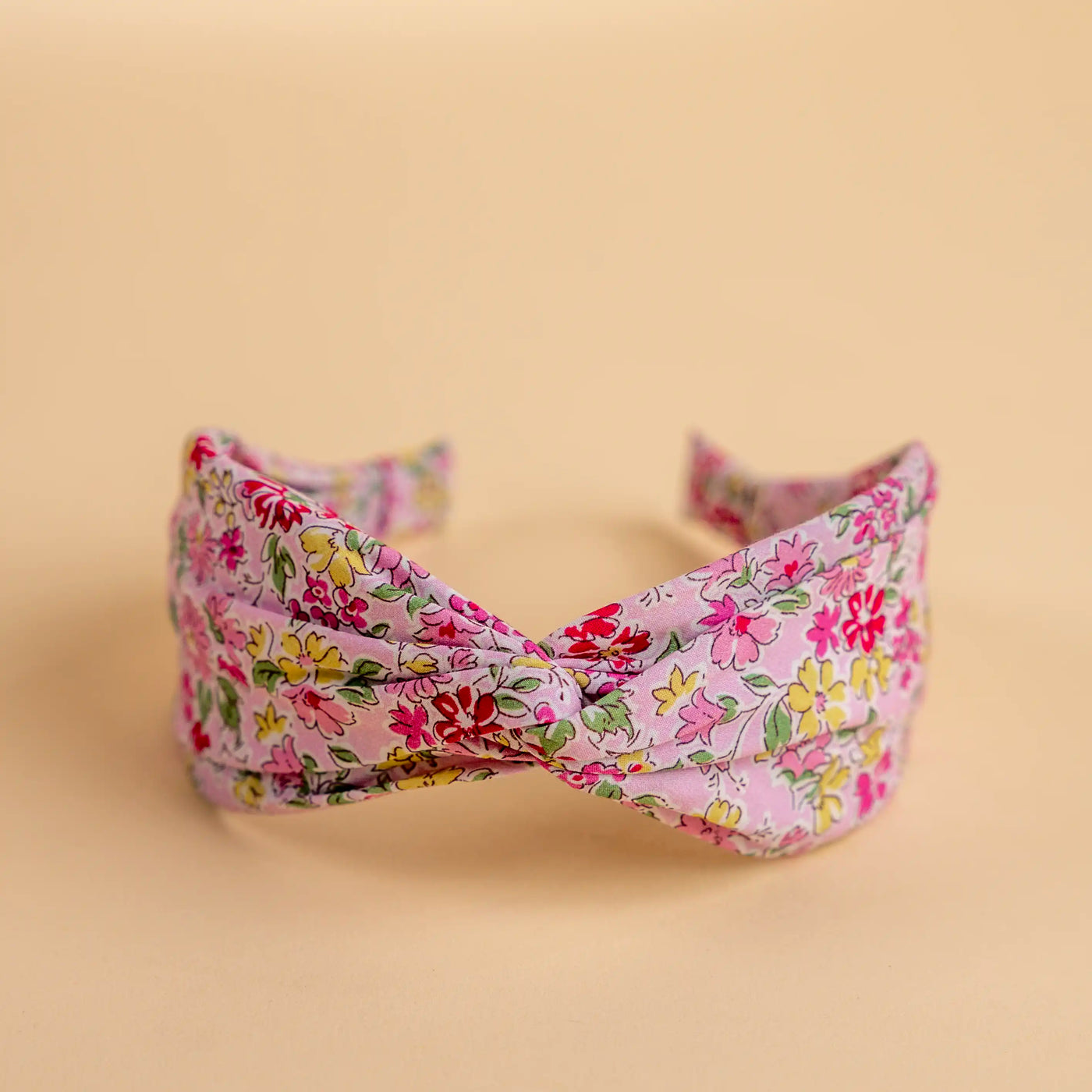 Lucys Pink Poppy Floral Headband. Light pink background with pink and yellow flowers. Front view. 