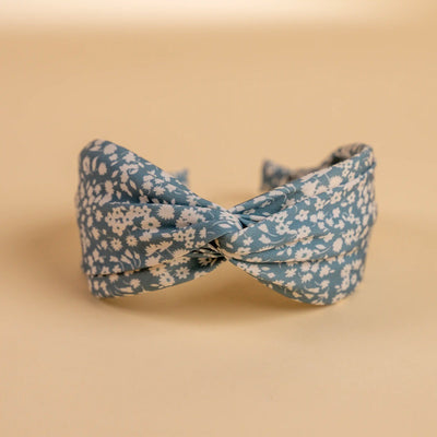 Lucys blue and white simple floral headband. Light blue background with simple white floral pattern. Front view. 