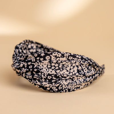 Lucys black and white simple floral headband. Black background with simple white floral pattern. Side view.